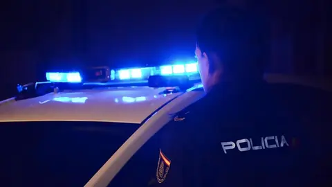 Un agente de la Polic&iacute;a Nacional, frente a un coche del cuerpo  con las luces de emergencia encendidas (fotograf&iacute;a/Polic&iacute;a Nacional).